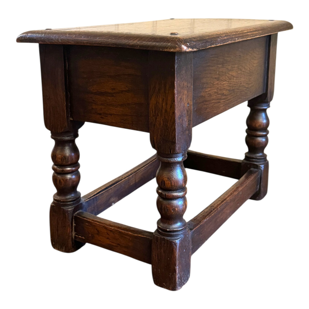 Rear three-quarter view of antique oak joint stool showing thick moulded top, turned legs and dark aged oak finish