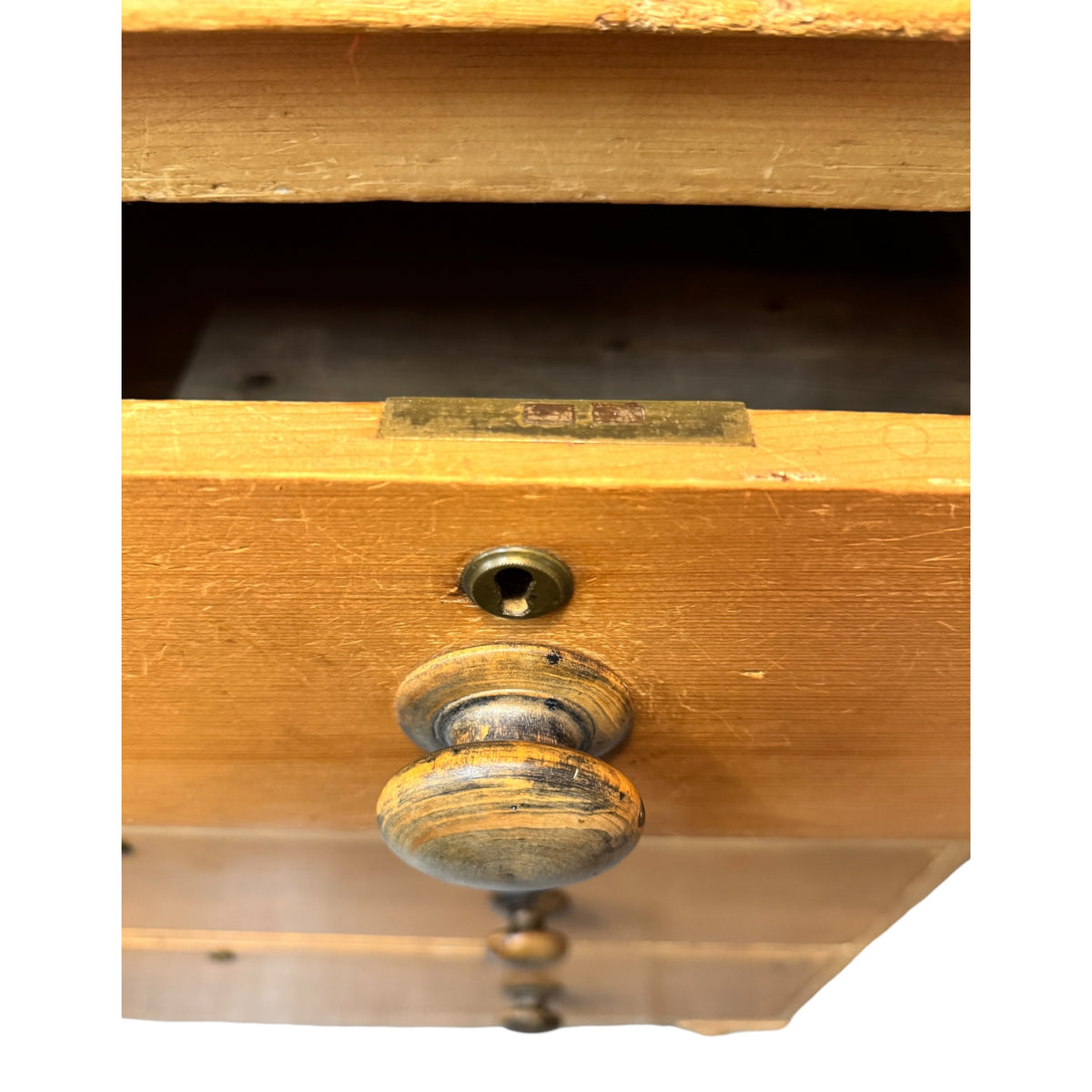 Close-up of antique drawer knob, brass escutcheon and lock on Victorian pine chest of drawers.