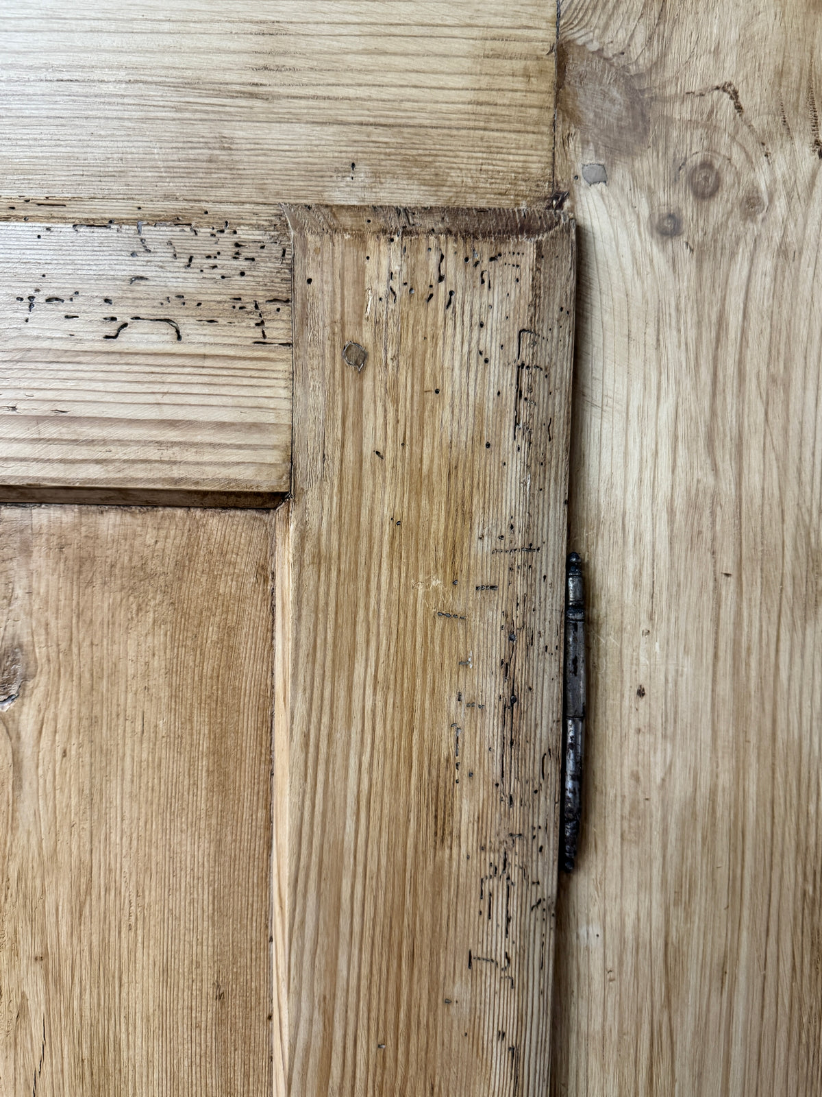 Close-up of traditional pine wardrobe door construction showing panelled joinery, iron hinge and historic surface wear