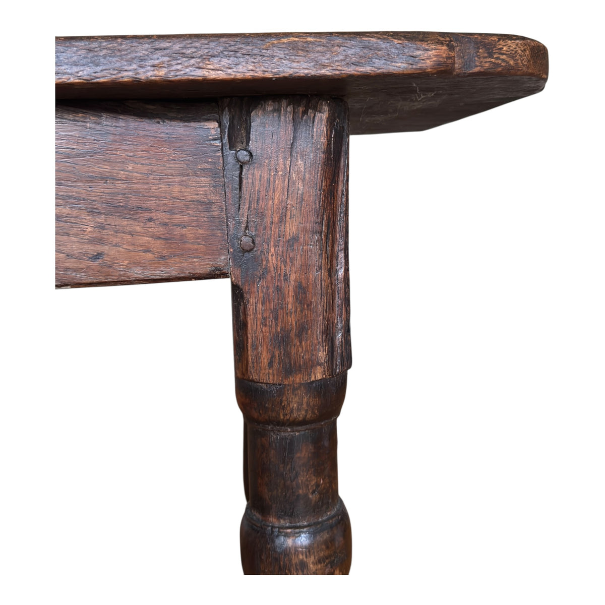 Close-up of the oak tavern table showing the junction between the frieze and turned leg, with old pegged construction and centuries of surface wear.