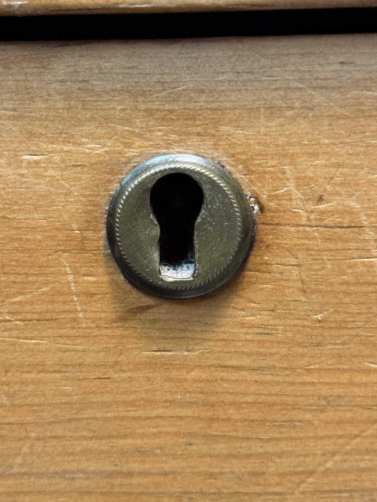 Close-up of round brass keyhole escutcheon on an antique Victorian pine drawer front.