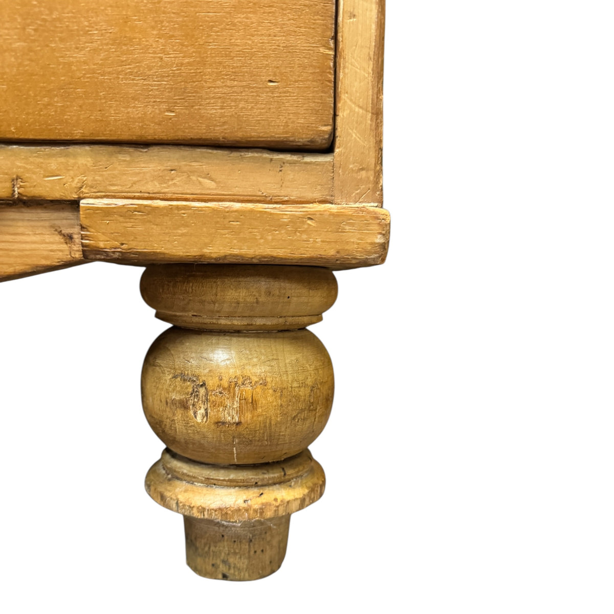 Close-up of turned wooden foot on antique Victorian pine chest of drawers showing age-related wear and patina.